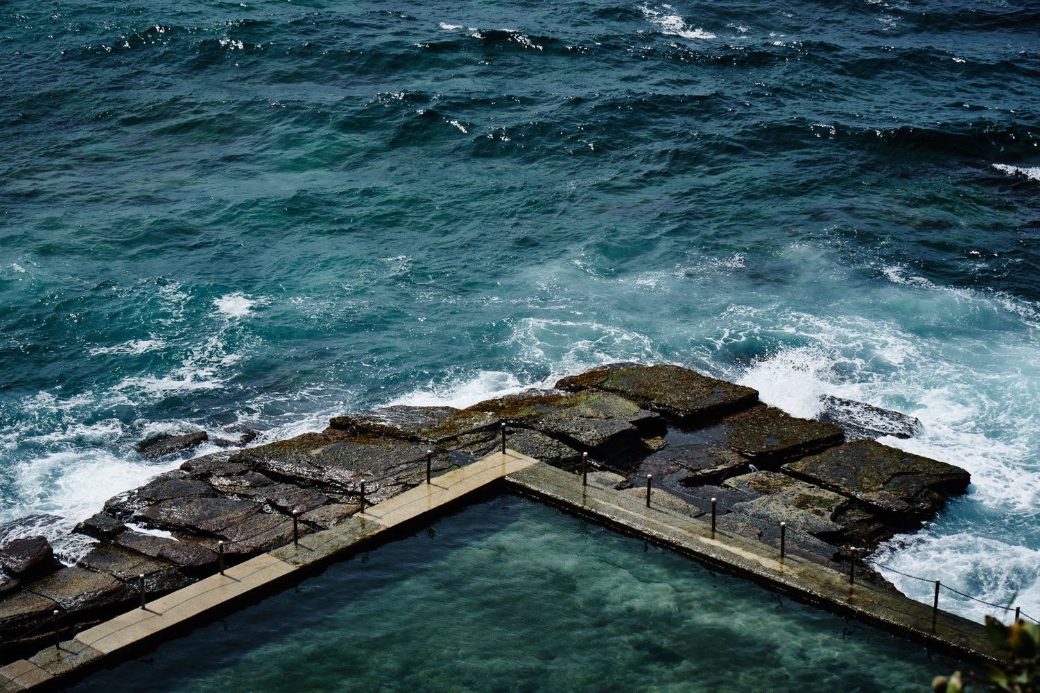 The ocean rock pool at Avalon Beach, with surf breaking across the rock shelf beyond it.